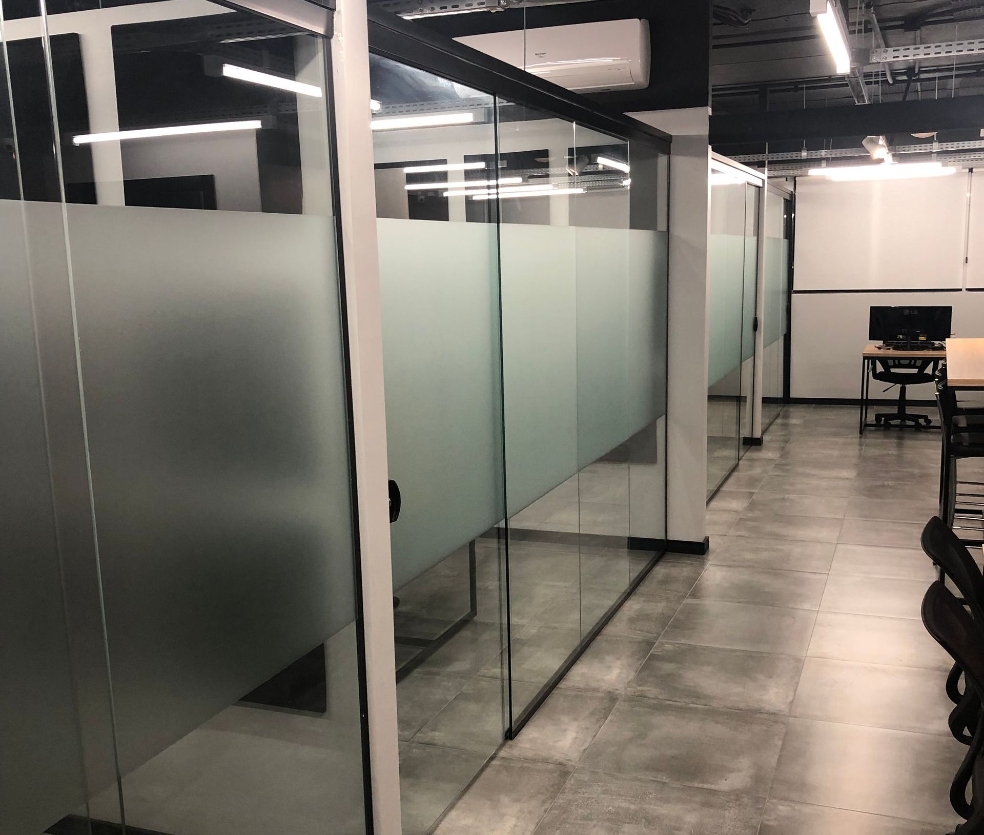 Uma sala com muitas paredes de vidro e uma escrivaninha no Sandbox Coworking