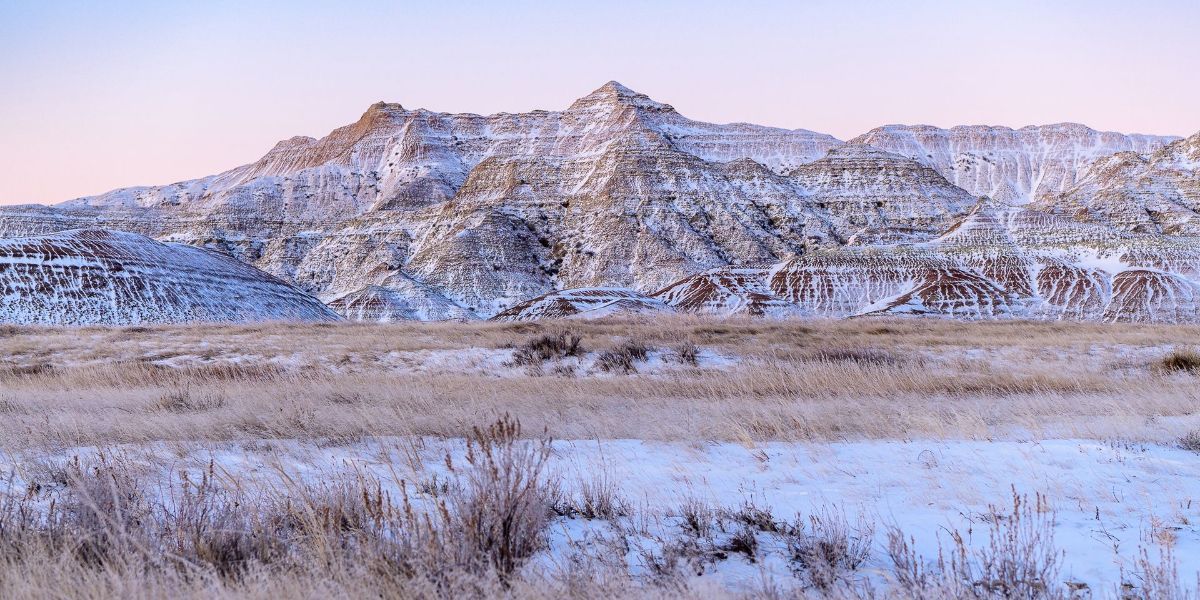 A snowy landscape with mountains in the background and a field in the foreground.