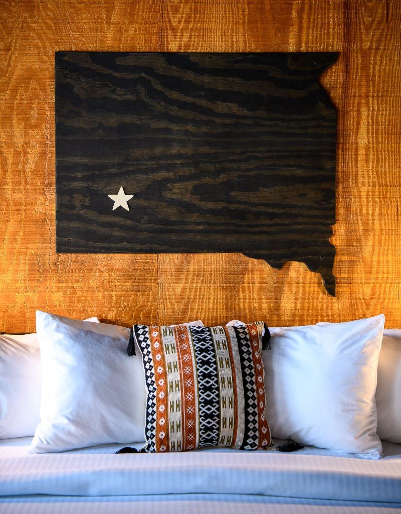 A bed with a wooden map of the state of texas on the wall above it