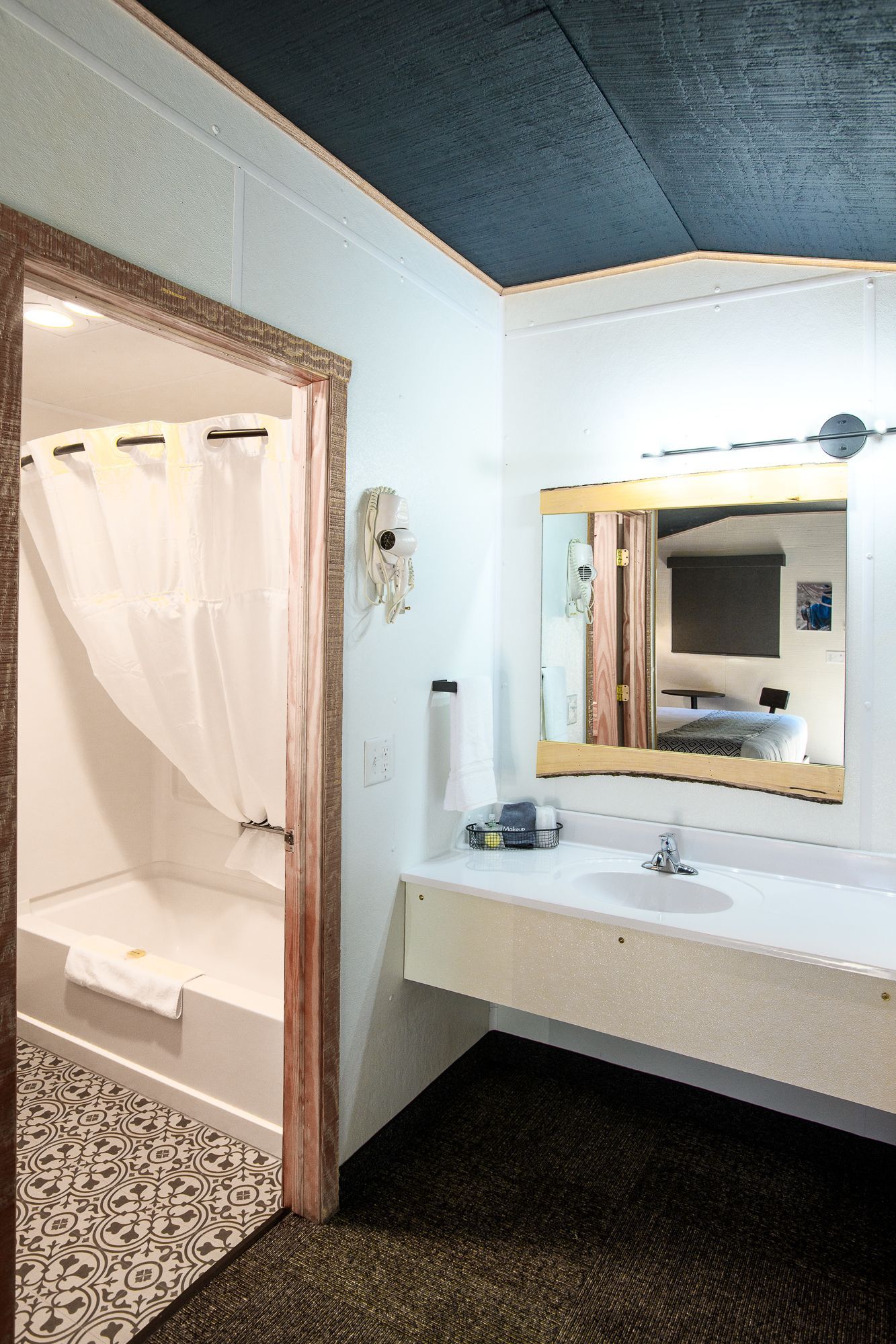 A bathroom in a hotel room with a sink , shower and mirror.