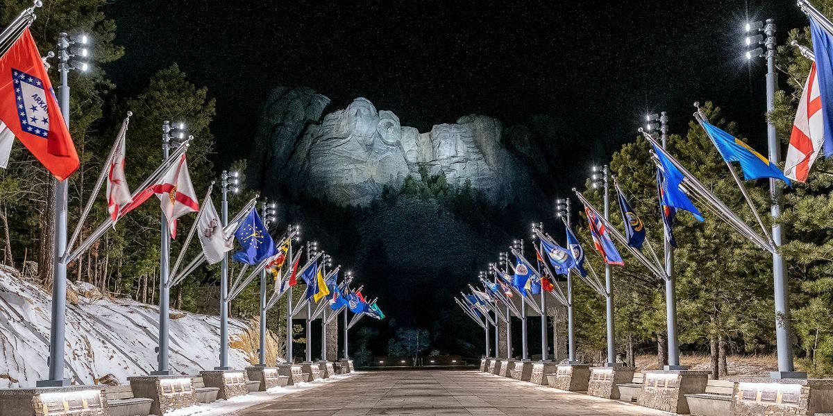 A row of flags are lined up in front of a mountain at night.