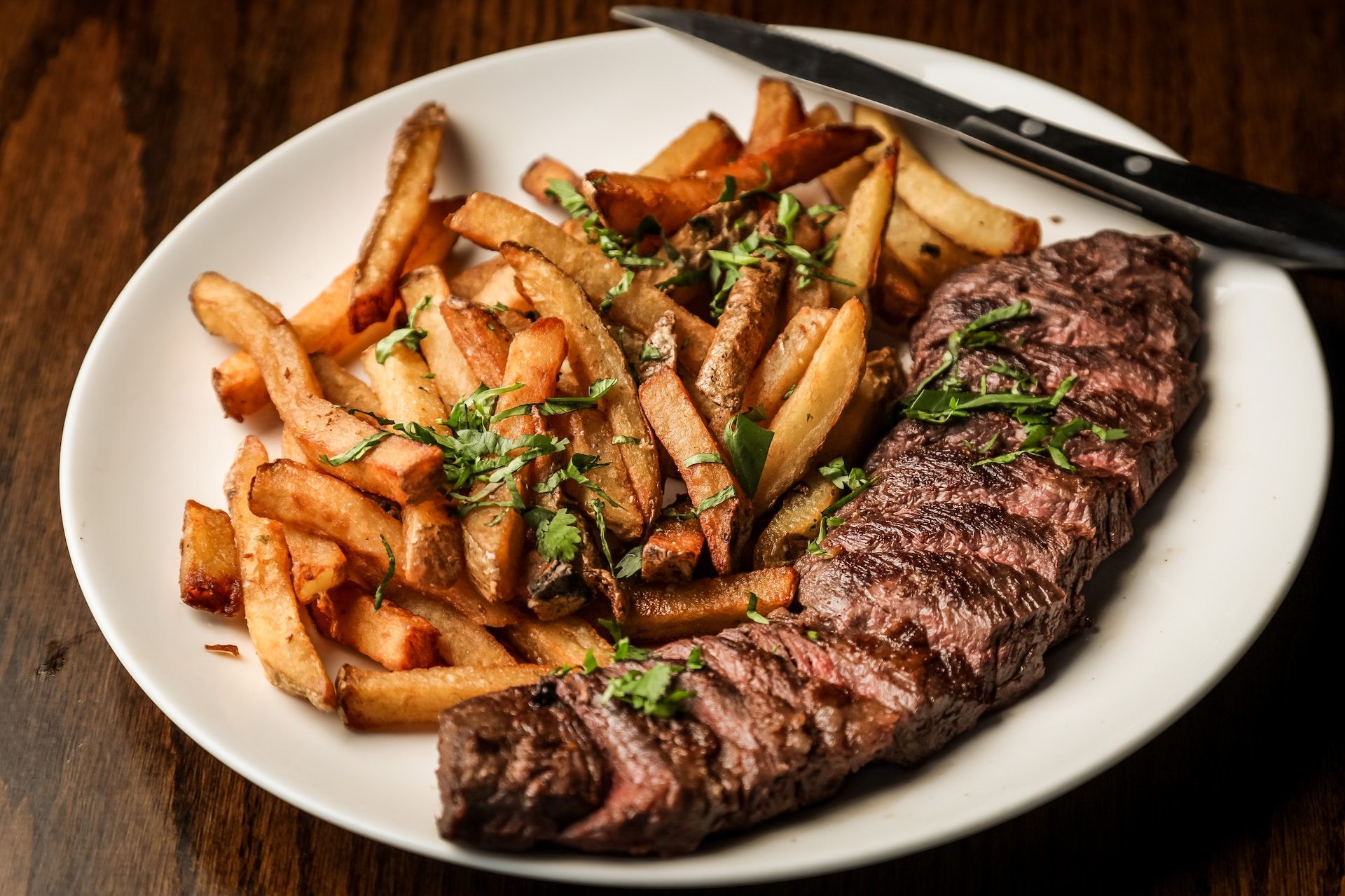 A white plate topped with steak and french fries on a wooden table.