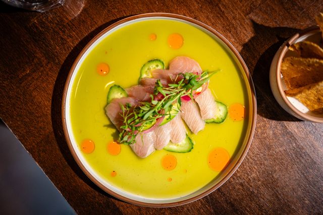 Bowl of green soup topped with sliced meat and herbs on a wooden table