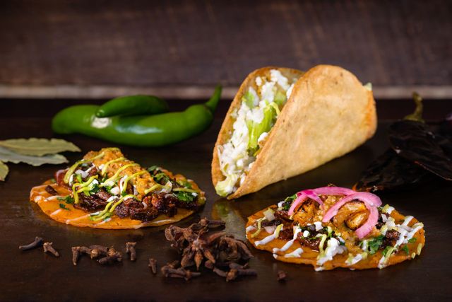 Assorted tacos on a dark table with green peppers in the background