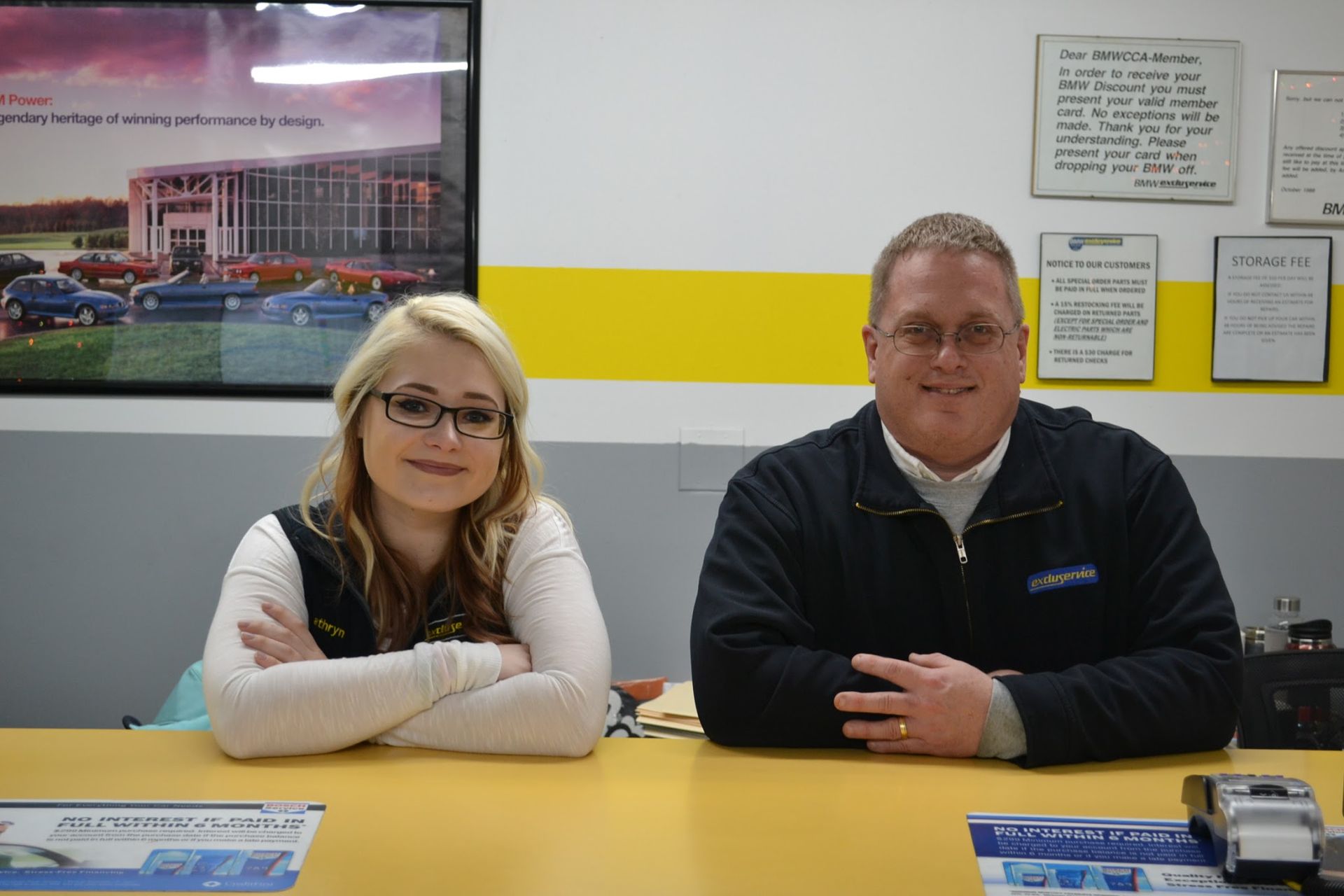 Woman and man sit at a yellow desk indoors | Excluservice
