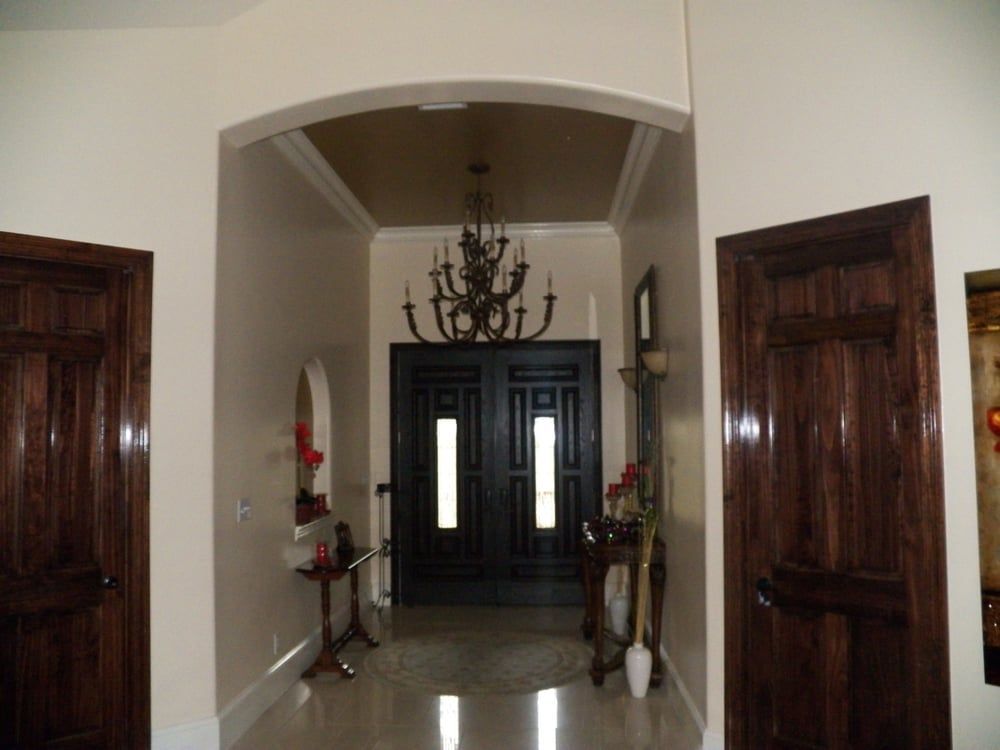 A hallway with a black door and a chandelier hanging from the ceiling