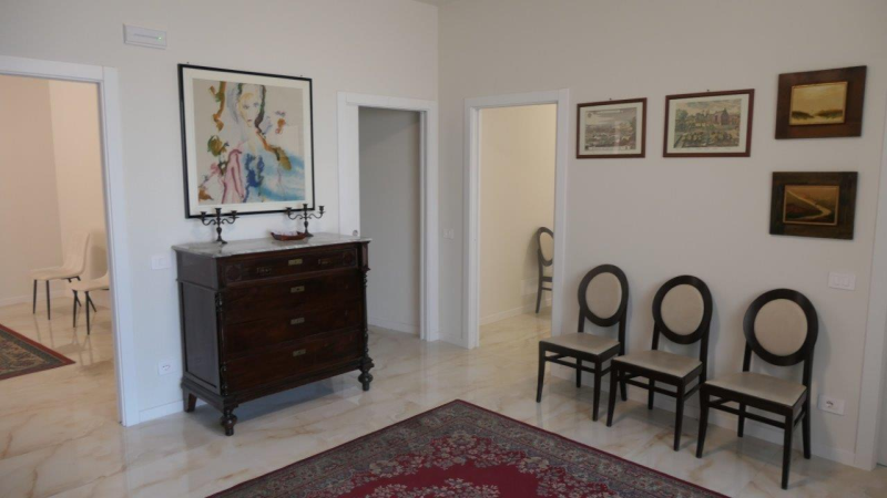 Accogliente sala d'attesa con divano giallo, poltrone scure, quadri incorniciati e una lampada da terra.