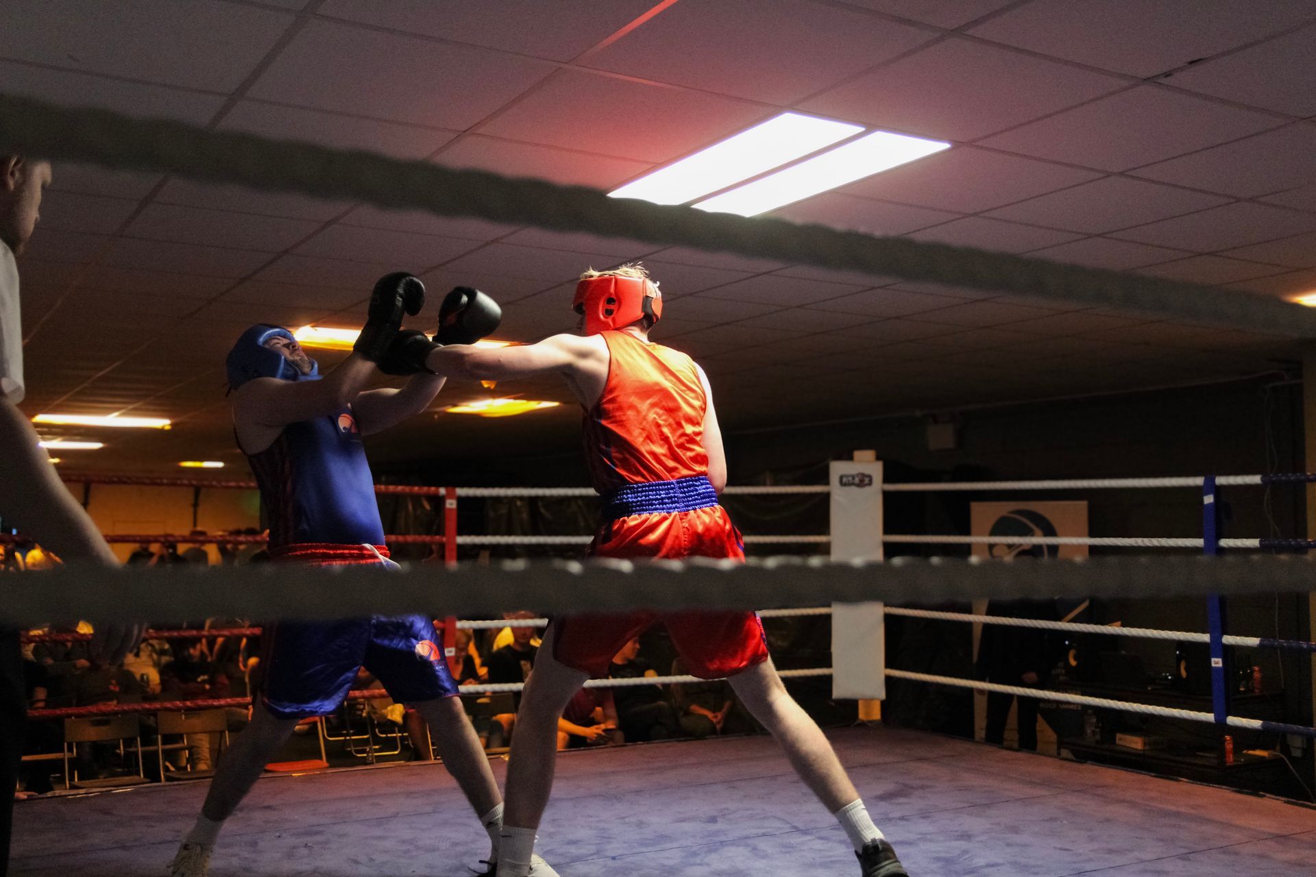 Two boxers in a ring; one throws a punch at the other. Red and blue uniforms.