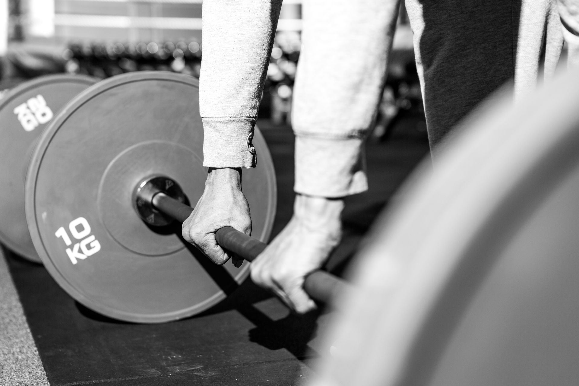 Person's hands gripping barbell, preparing to lift. Two 10 kg weights attached, gym setting.