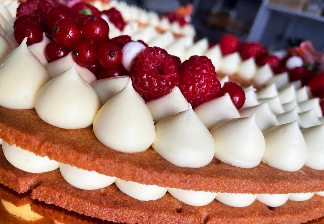 Primo piano di un dessert a strati con panna, frutti rossi e una base marrone chiaro.