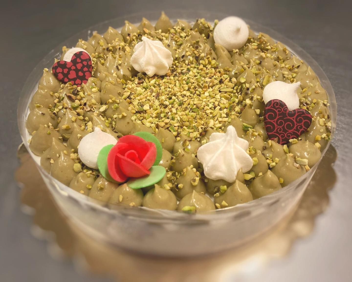 Torta al pistacchio ricoperta di glassa verde, pistacchi tritati, gocce di meringa e decorazioni di cioccolato a forma di cuore.