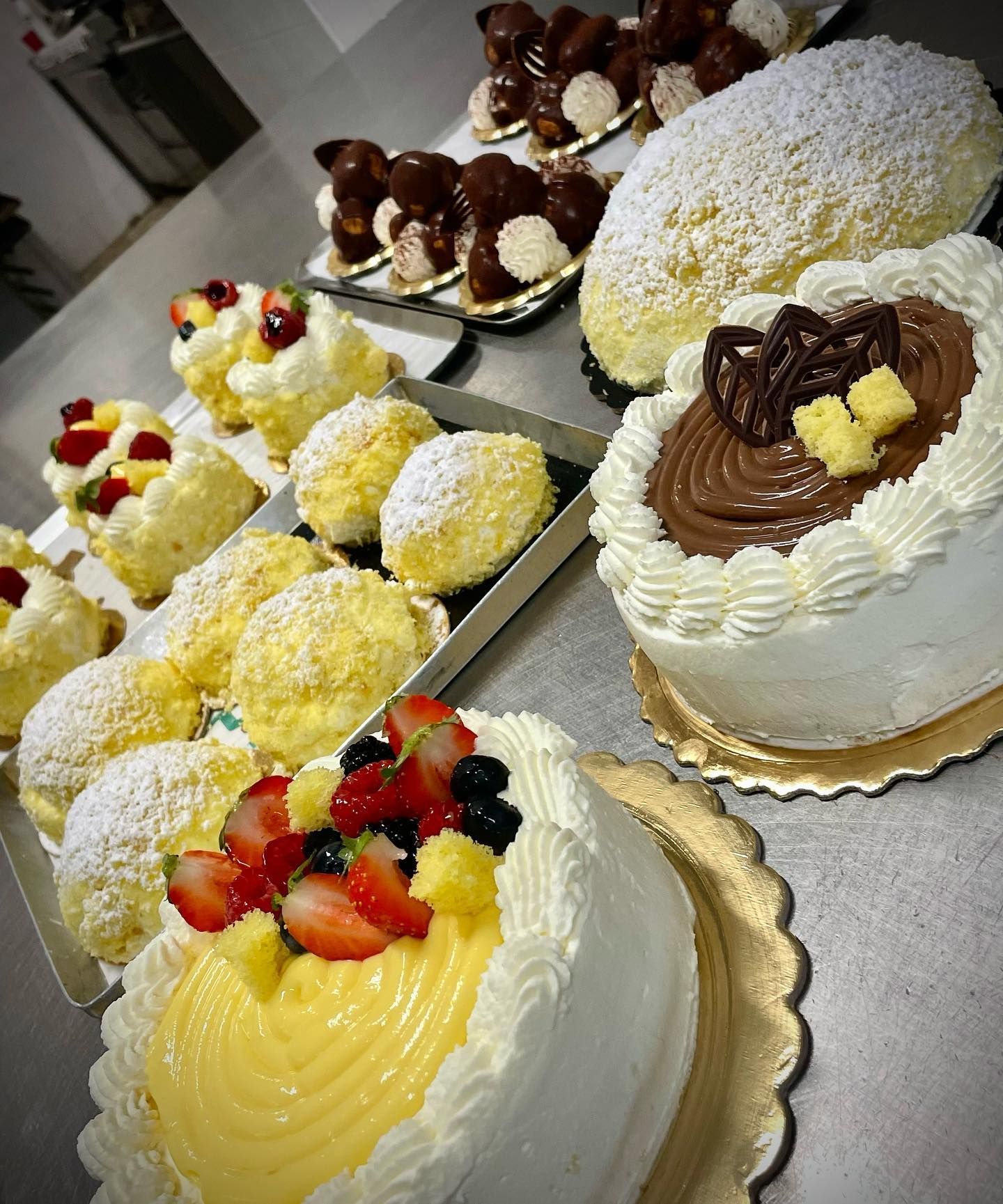 Assortimento di pasticceria italiana: torte e bignè con guarnizioni di frutta e cioccolato, disposti su un bancone.