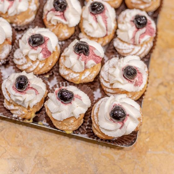 Vassoio di bignè con panna montata, una ciliegia e zucchero a velo su una superficie di marmo.