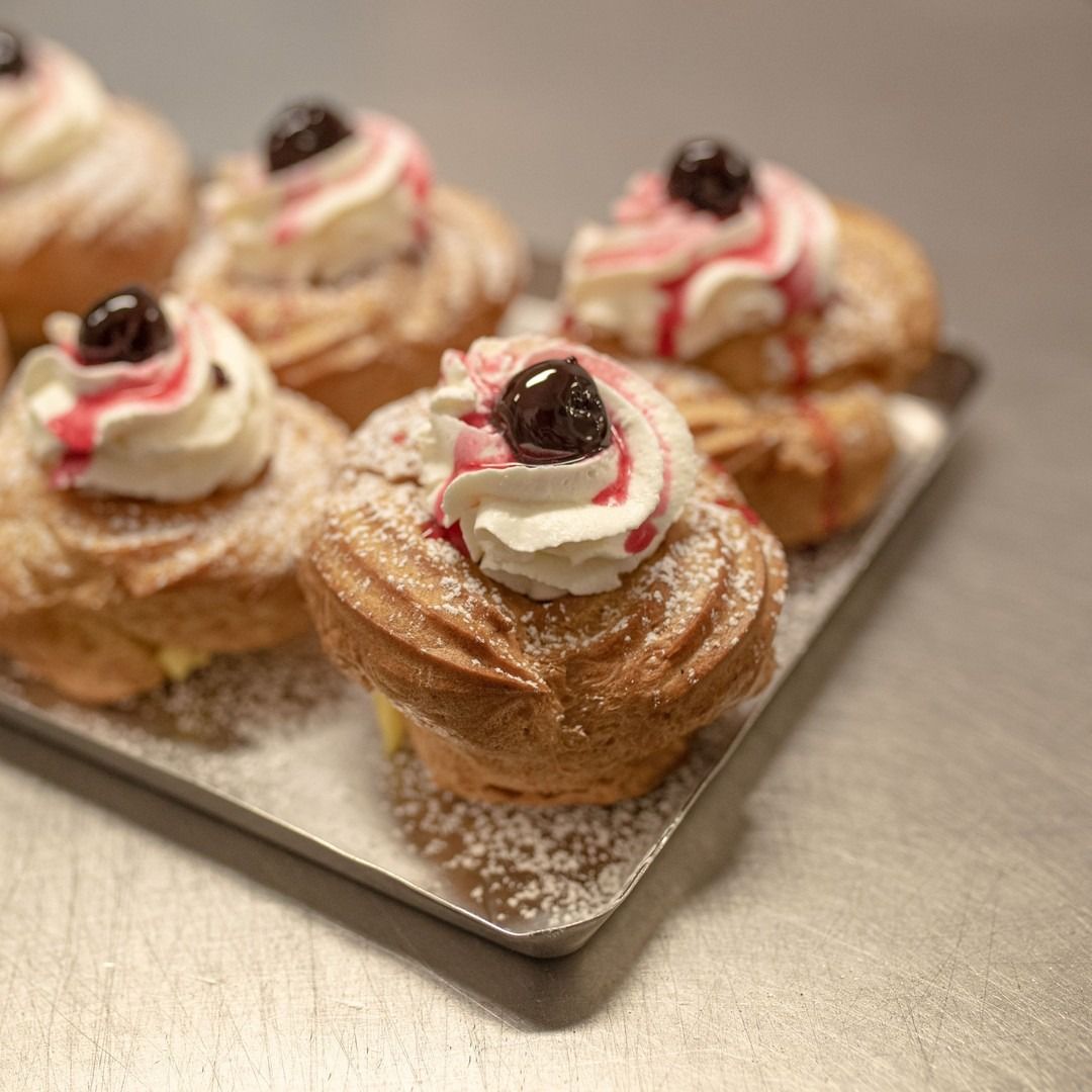 Vassoio di pasticcini guarnito con panna montata, una ciliegia e sciroppo rosso, spolverato con zucchero a velo.