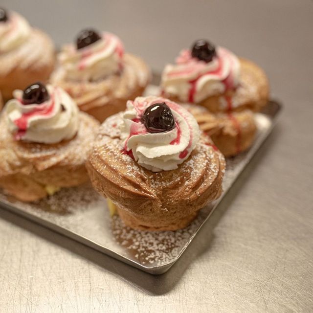 Vassoio di pasticcini guarnito con panna montata, una ciliegia e sciroppo rosso, spolverato con zucchero a velo.
