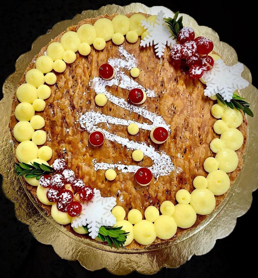 Una torta natalizia decorata con un bordo color crema, grappoli di mirtilli rossi zuccherati e un albero di Natale ricoperto di zucchero a velo.