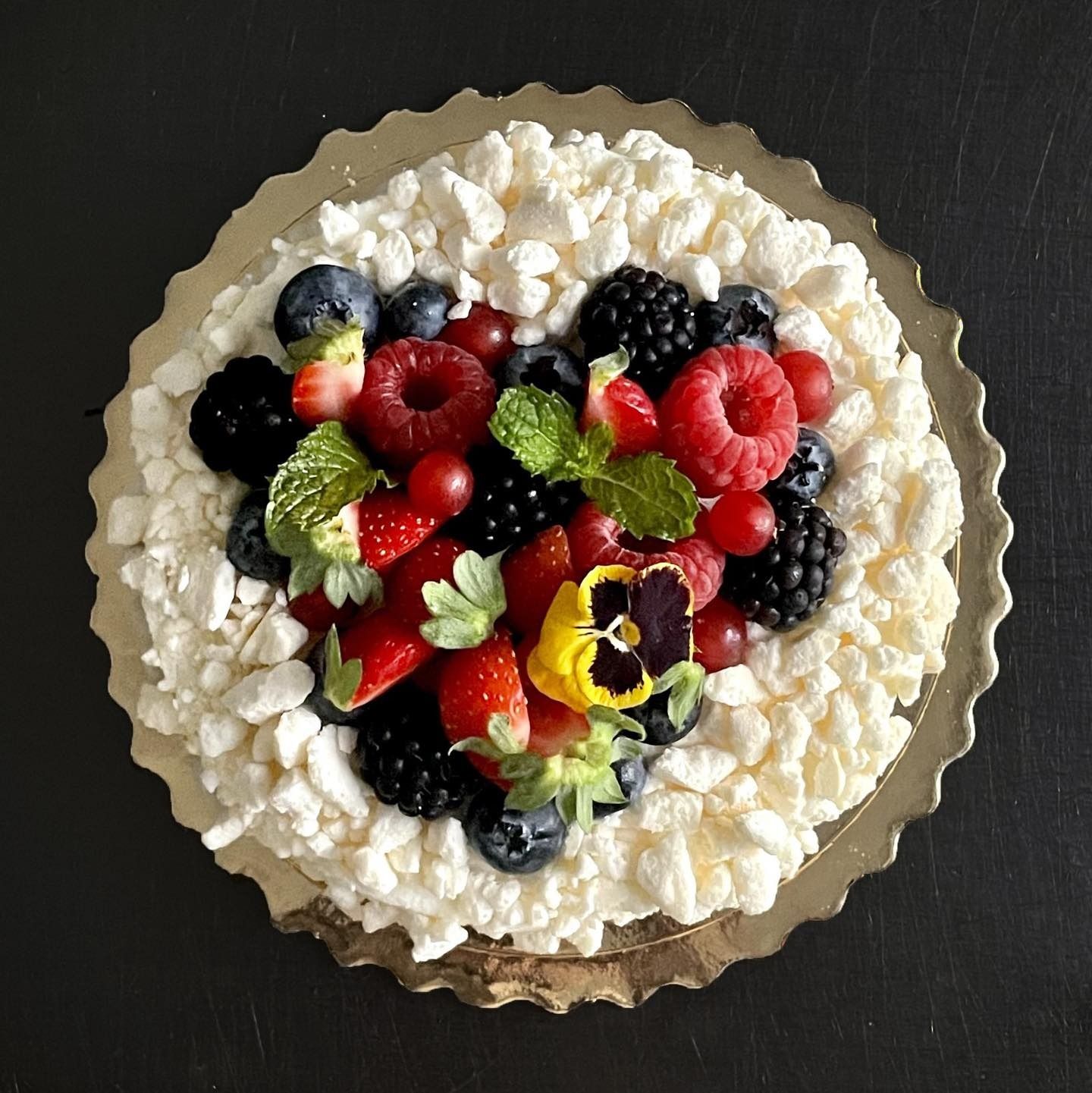 Dolce Pavlova con copertura di meringa montata e frutti di bosco misti, servito su un piatto da portata color oro.