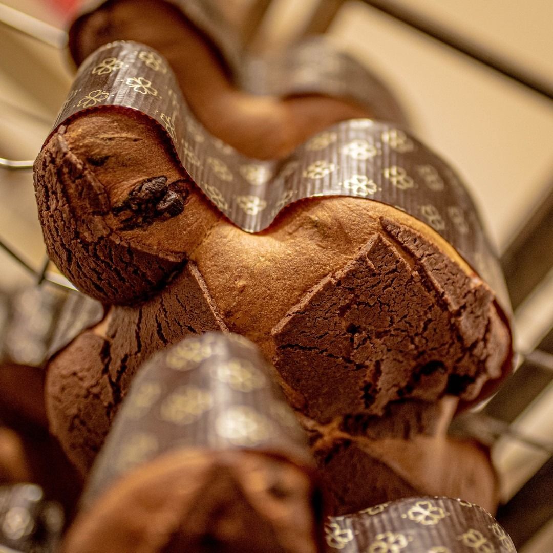 Primo piano di diversi panettoni dorati avvolti in involucri di carta, impilati su uno scaffale.