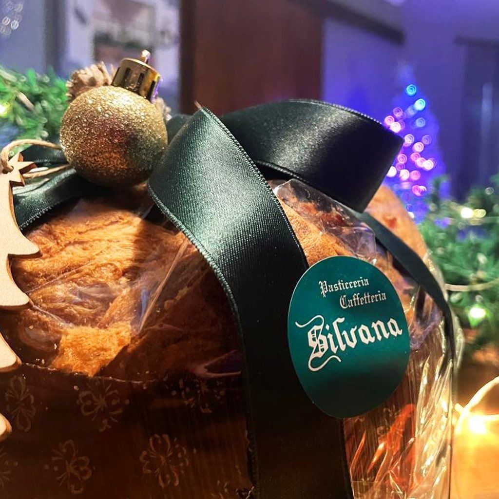 Primo piano di un panettone confezionato con un nastro verde e un adesivo della Pasticceria Silvana, decorato con un ornamento natalizio.