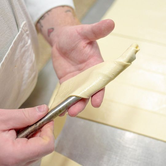 Un fornaio avvolge l'impasto della pasta frolla attorno a un cono di metallo, preparando un corno di pasta.