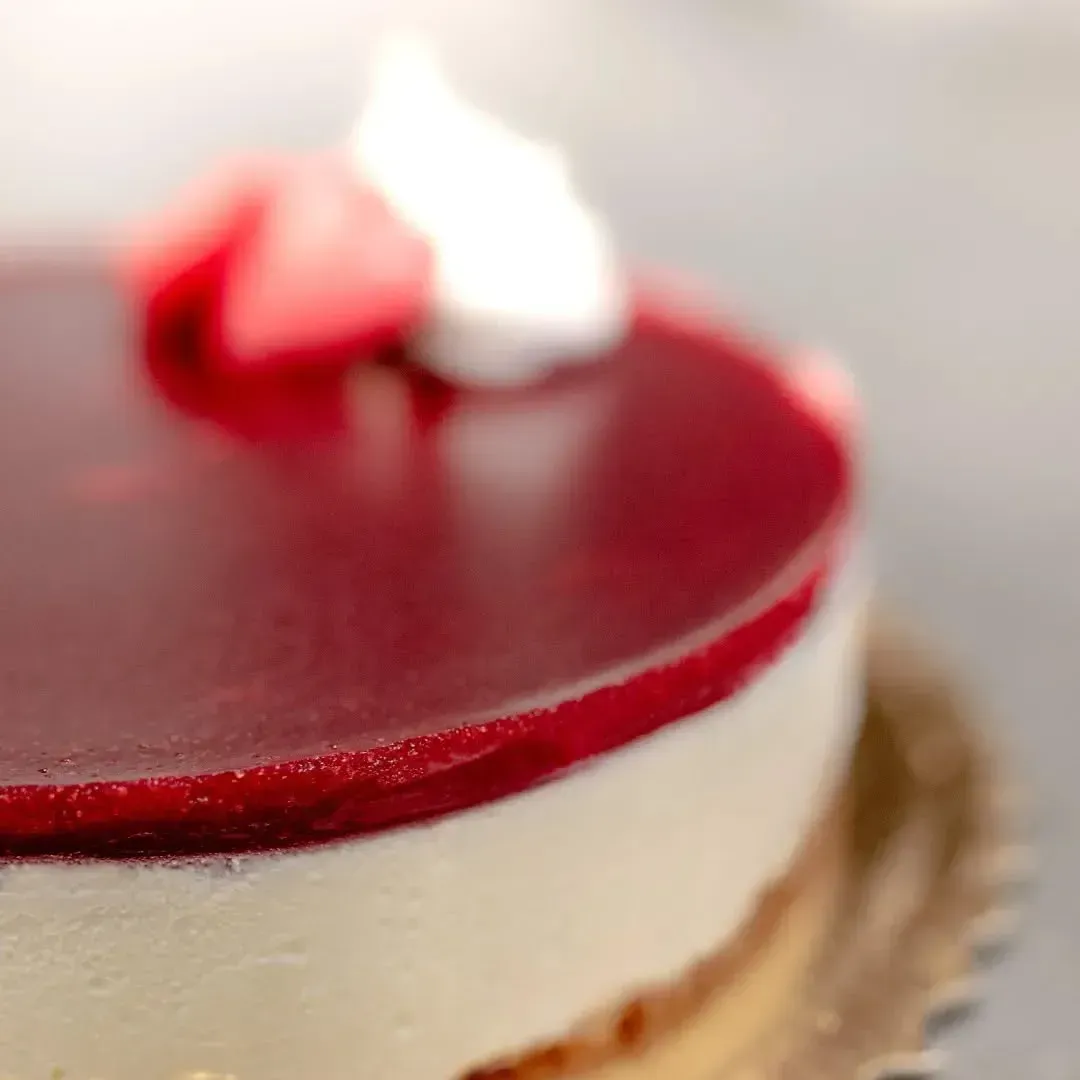 Cheesecake con glassa rossa, guarnita con una fragola e panna montata.