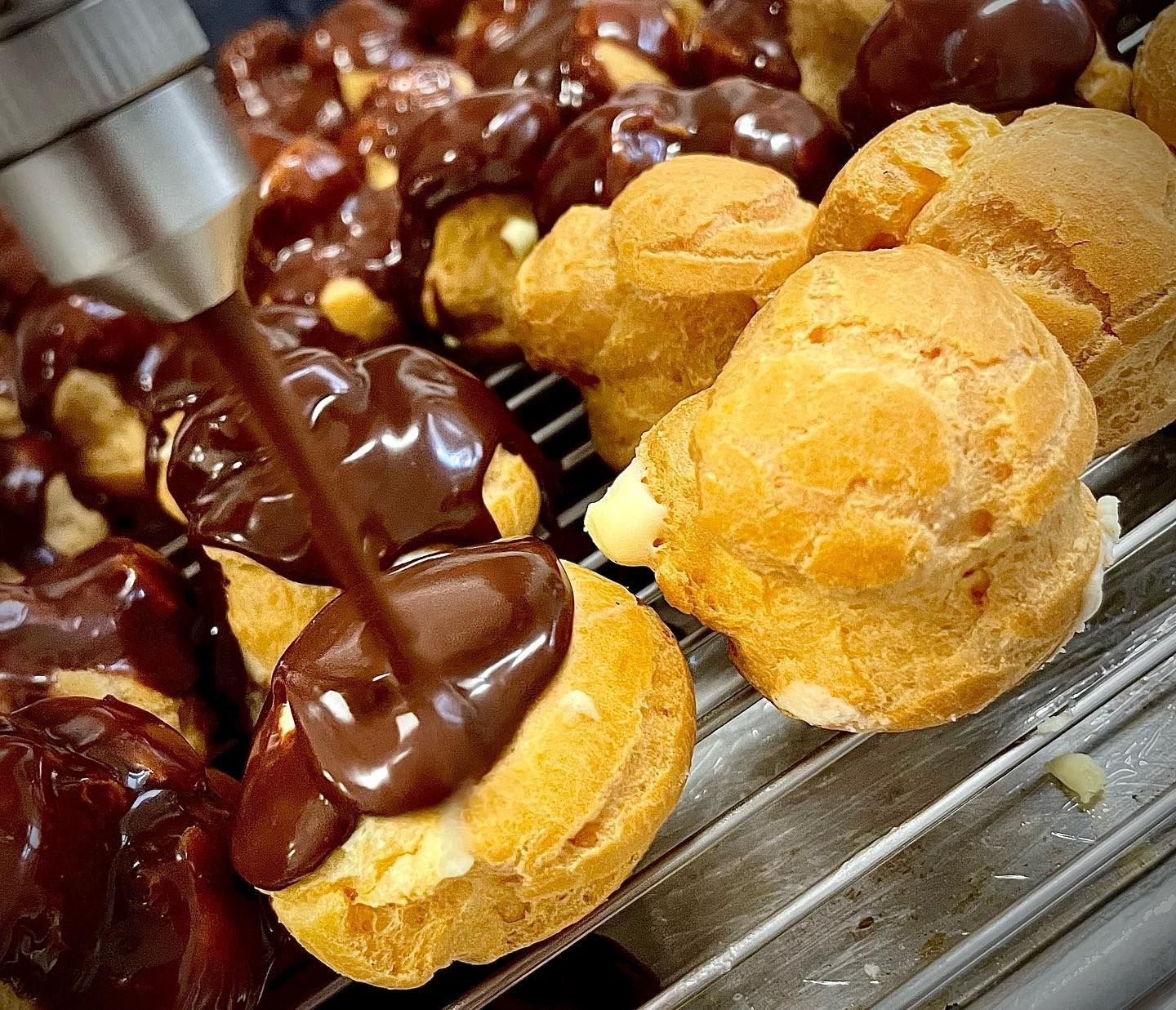Profiteroles ricoperti di salsa al cioccolato su una griglia di raffreddamento. I pasticcini sono dorati e la salsa è di un ricco marrone scuro.