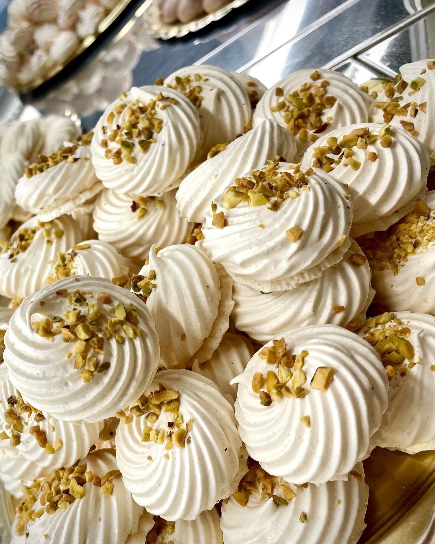 Biscotti di meringa bianchi e vorticosi, ricoperti di noci tritate, ammucchiati su un vassoio.