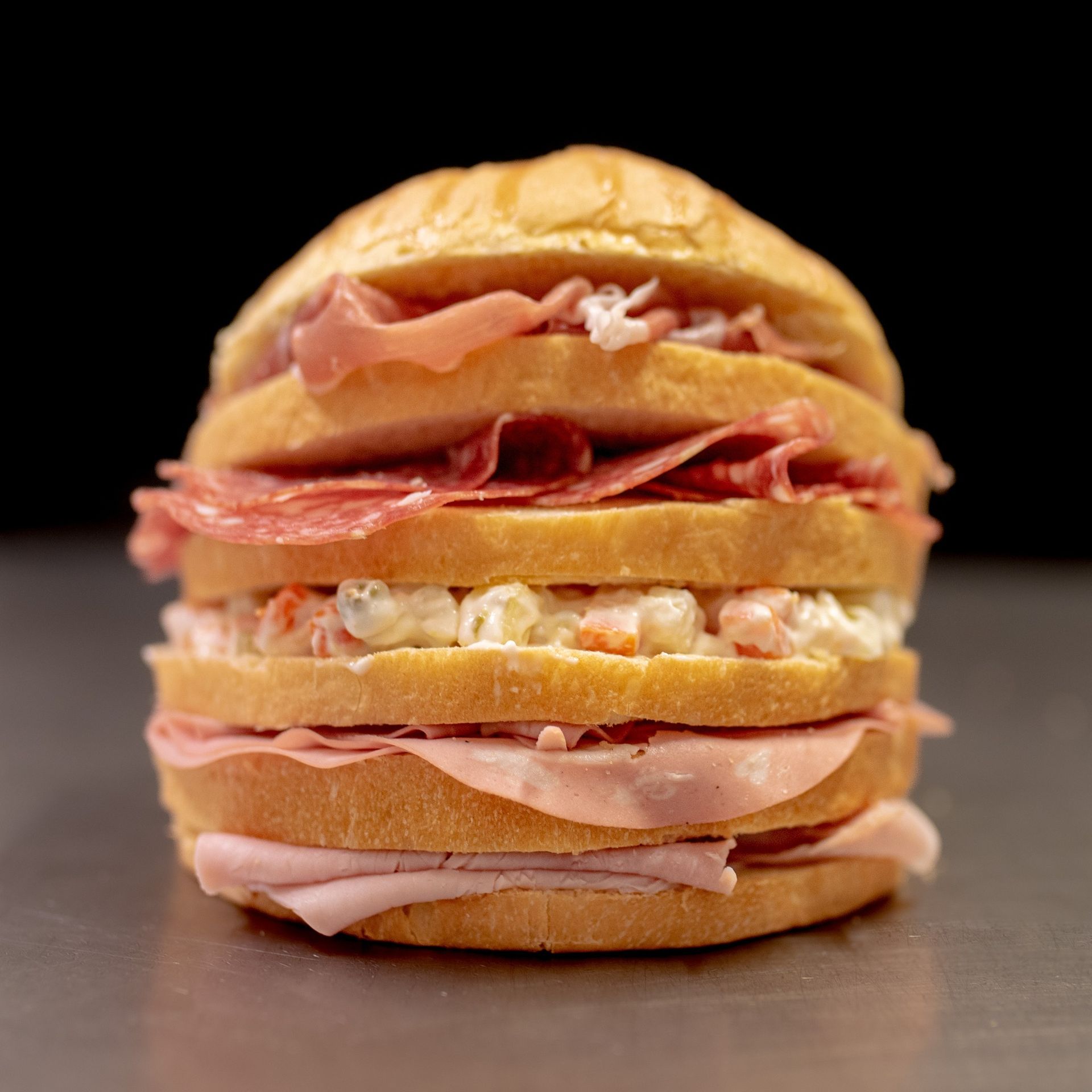 Panino farcito con mortadella, salame, insalata di patate e un panino, su sfondo nero.