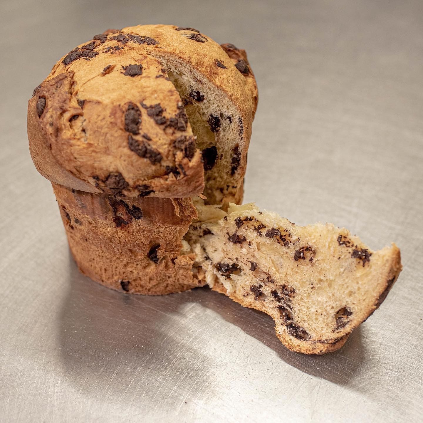 Muffin con gocce di cioccolato, parzialmente aperto, che rivela un interno morbido e strutturato, adagiato su una superficie di colore chiaro.