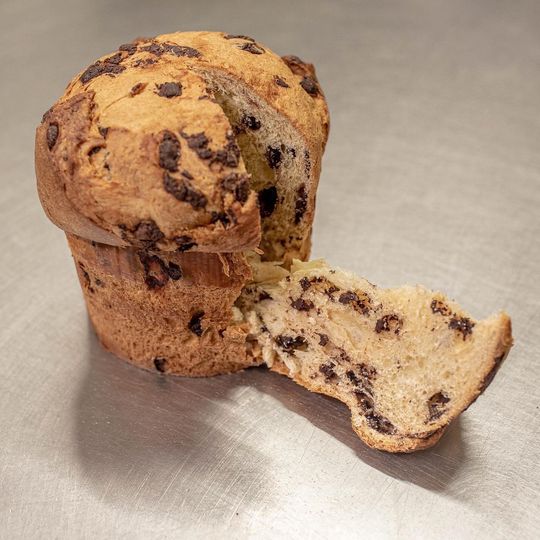Chocolate chip muffin, partially opened, revealing a soft, textured interior lying on a light-coloured surface.