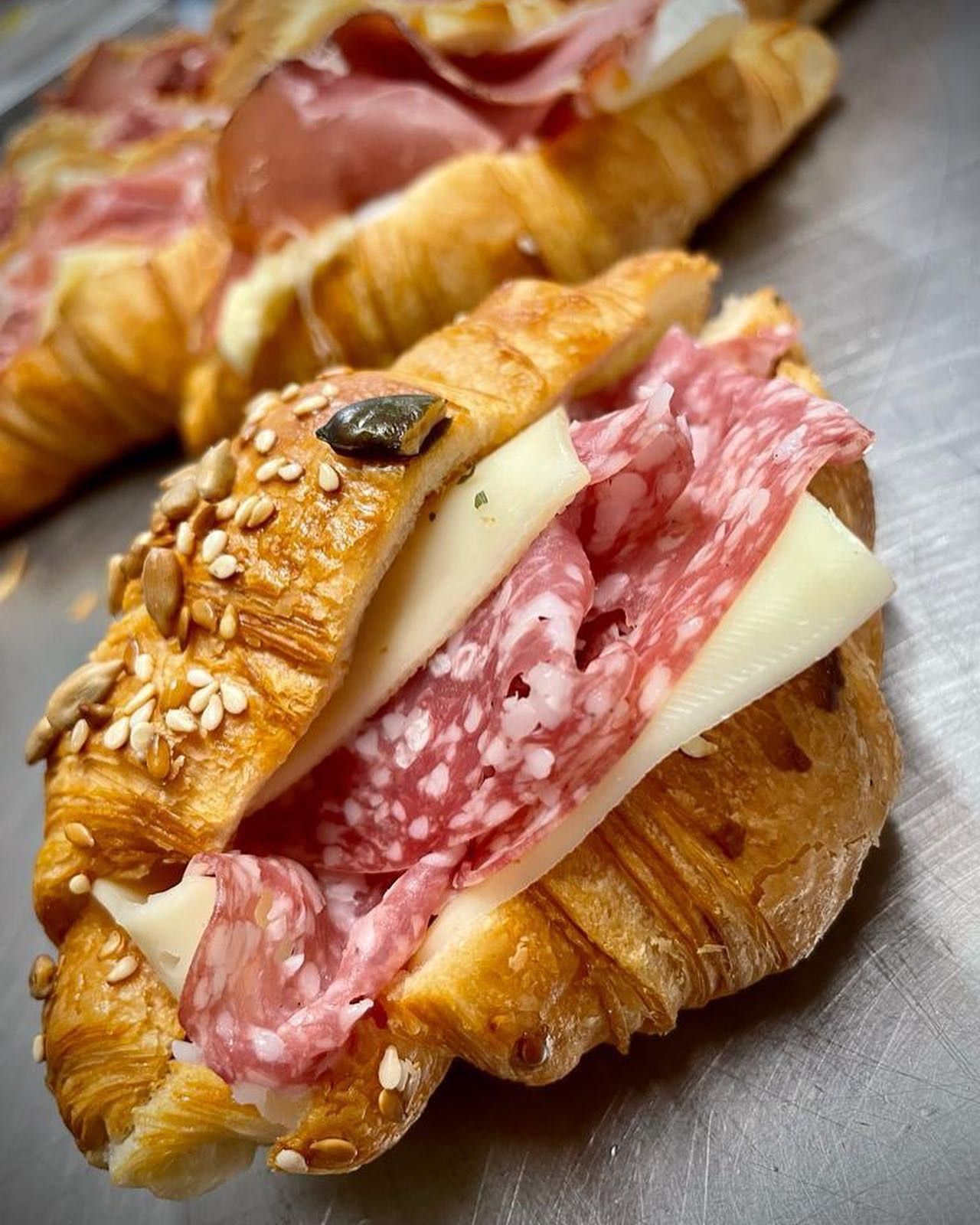 Croissant con salame e formaggio. Il pane ha semi in superficie e una forma leggermente ripiegata.