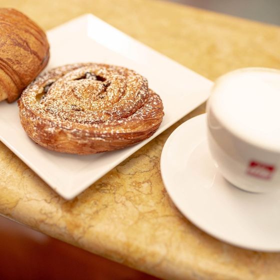Pasticcini e una tazza di caffè su un bancone. Un croissant e un dolce a spirale sono su un piatto, e una tazza di caffè è su un piattino.