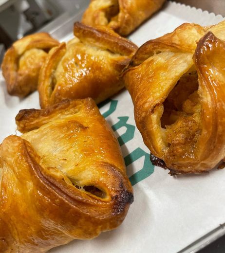 Dei dolcetti dorati e sfogliati, magari dei fagottini o simili, sono adagiati su un foglio di carta bianca con un logo verde, sistemato su un vassoio.