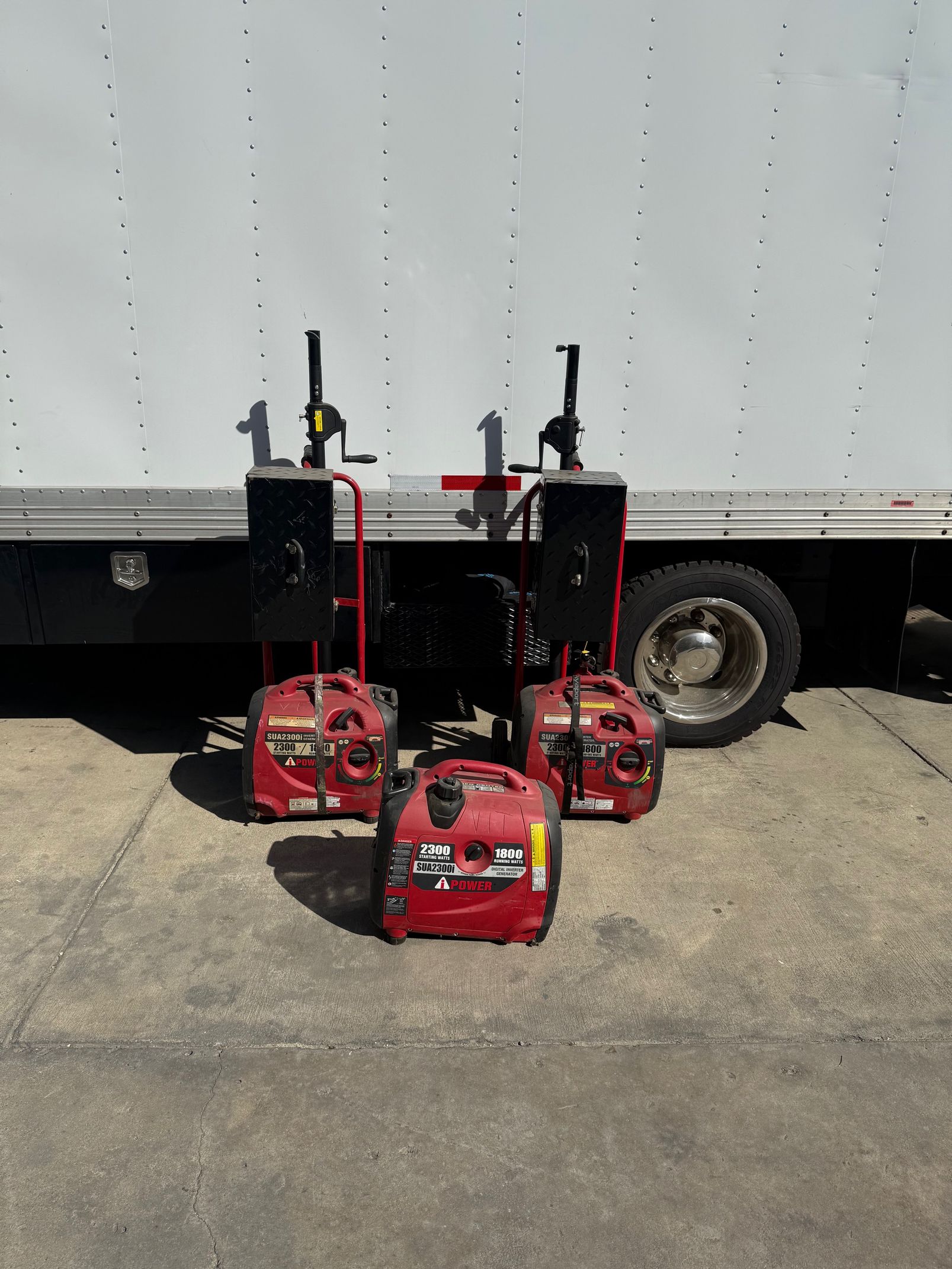 Four red generators on a concrete surface in front of a white truck.