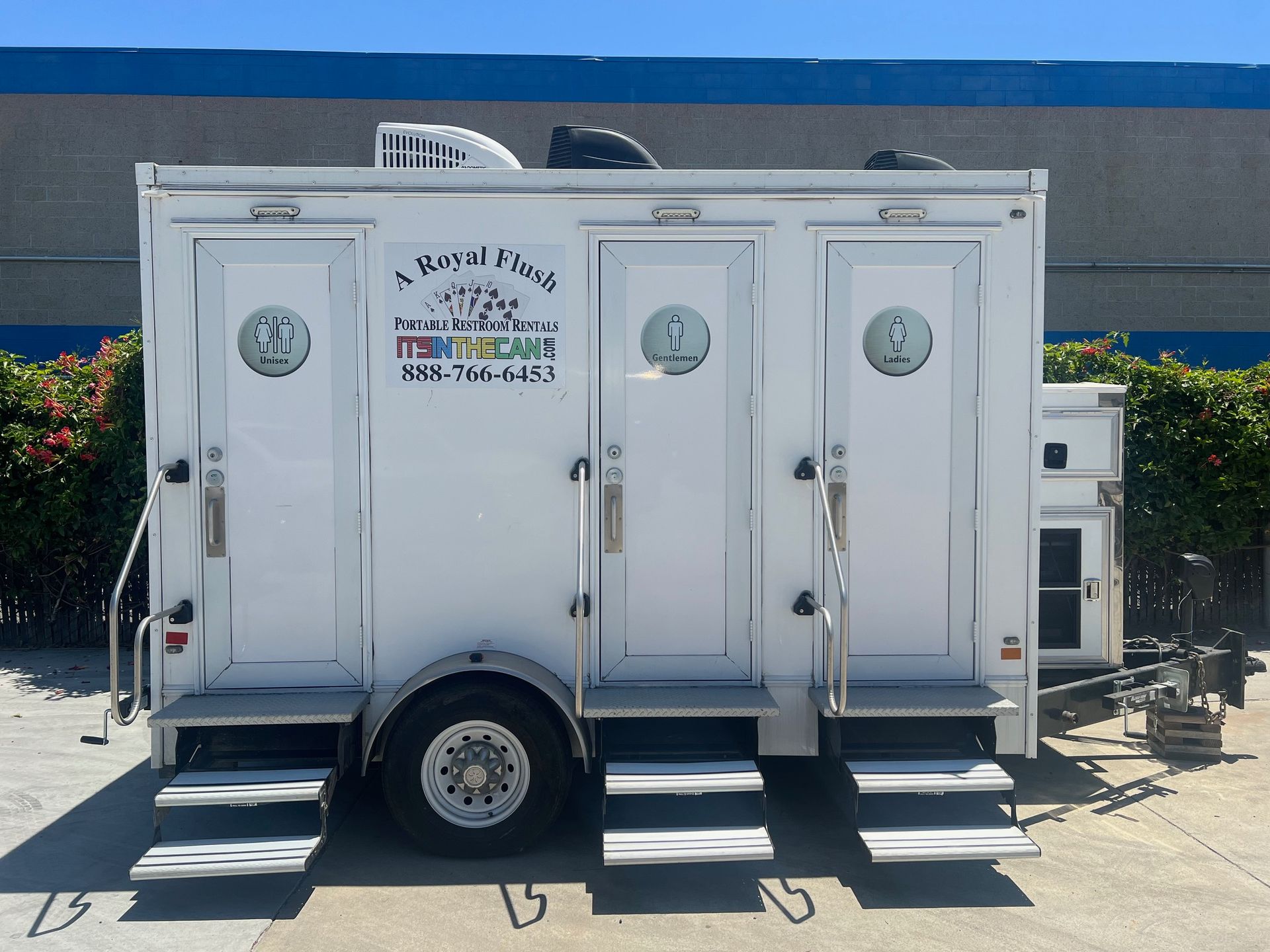 White portable restroom trailer with three individual stalls; parked outdoors.