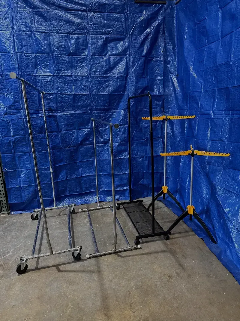 Three clothing racks on wheels in front of a blue tarp.