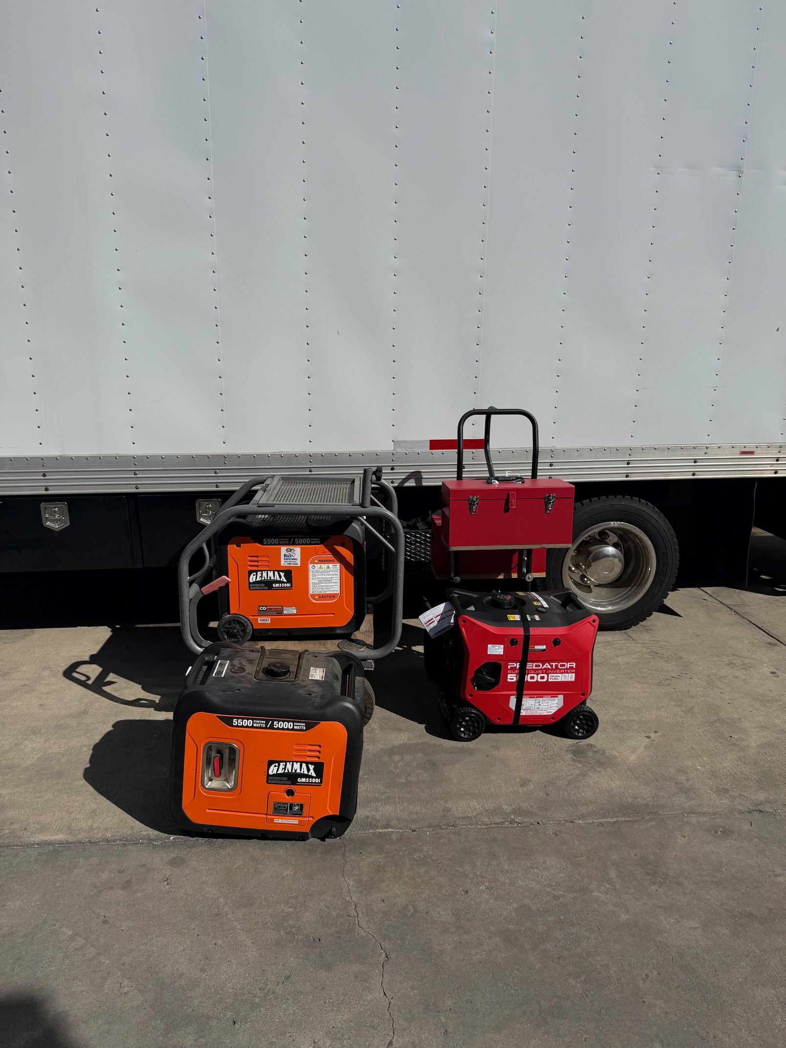 Three portable generators; two orange, one red, in front of a truck.