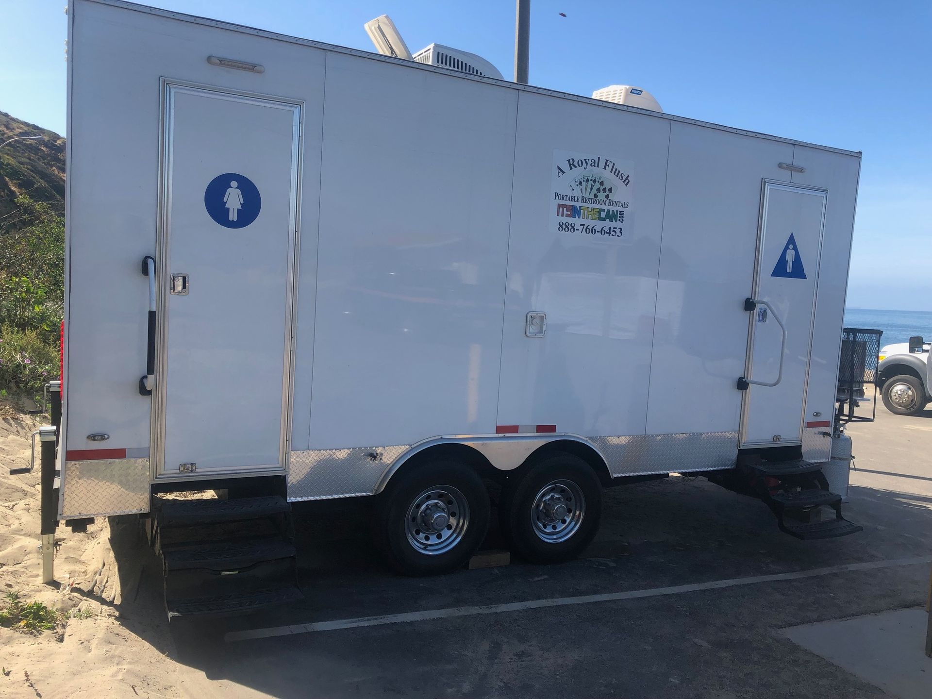 White portable restroom trailer with two doors, near beach.