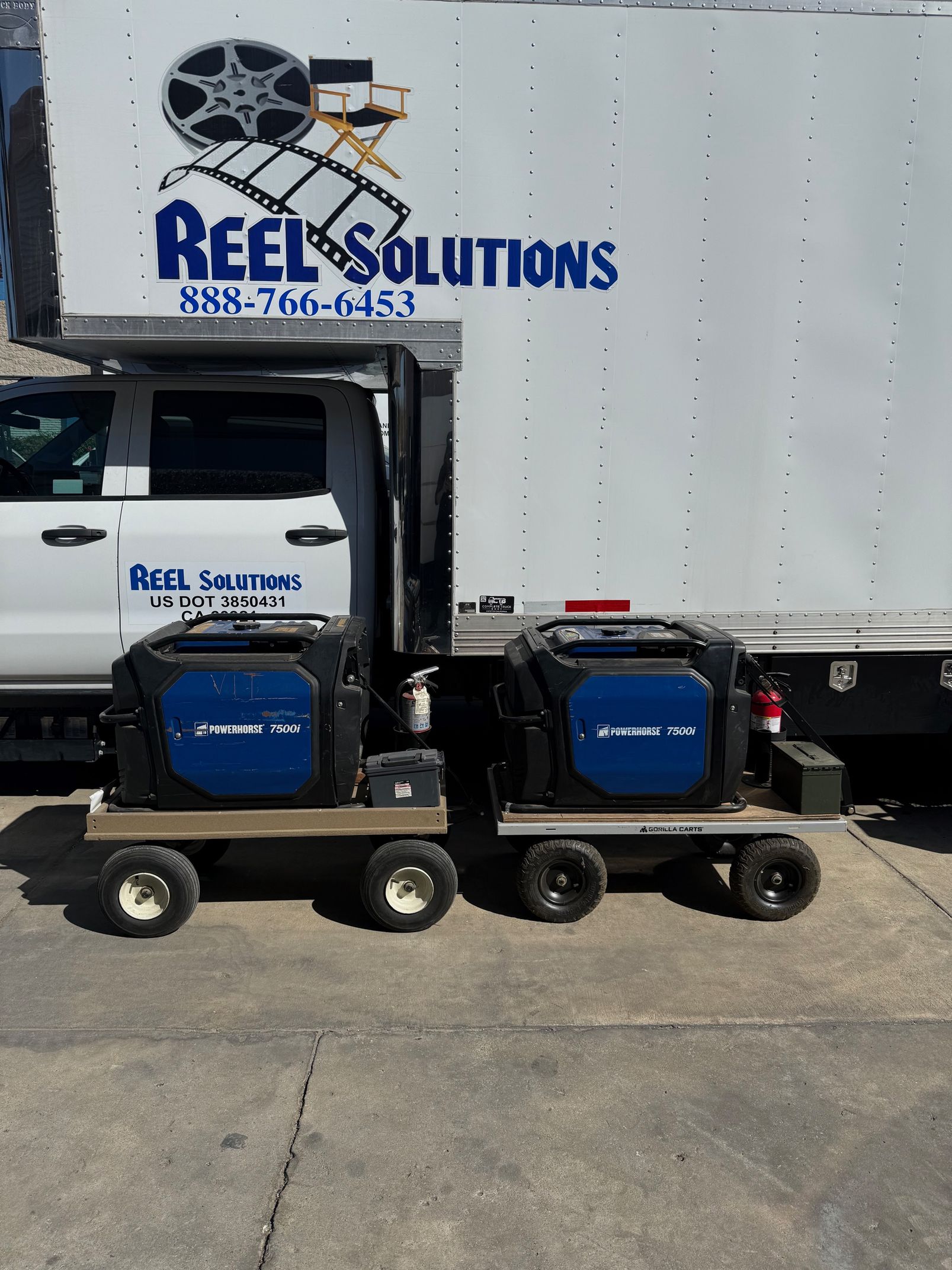 Two blue generators on wheeled carts, in front of a white truck with 