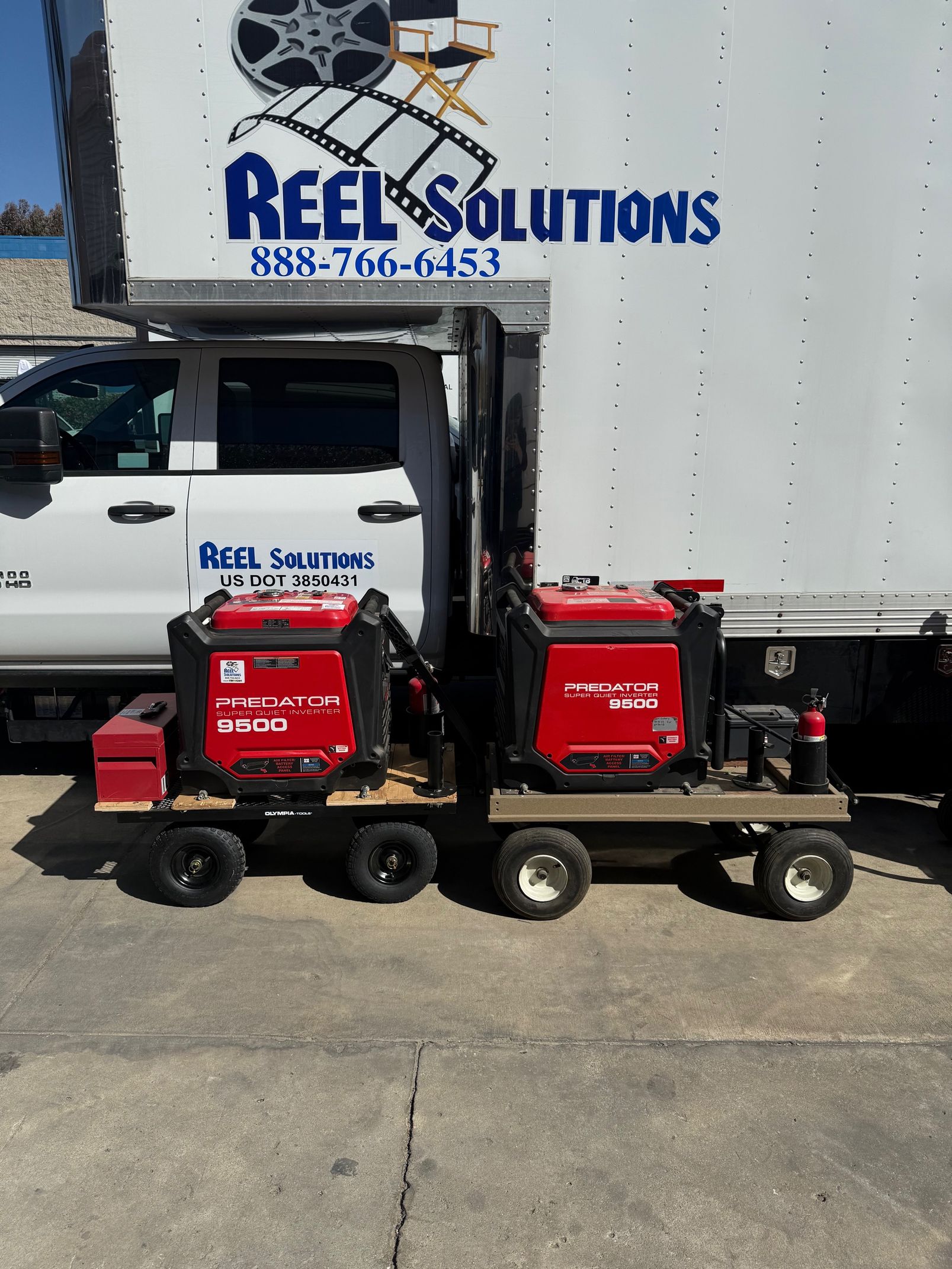 Two red welding machines on carts in front of a truck with 