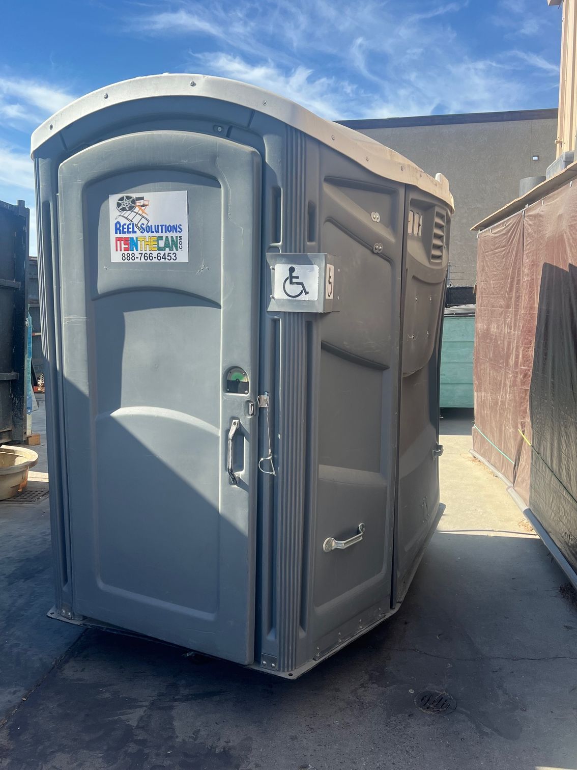 Gray, accessible portable toilet with a wheelchair symbol and door handle.
