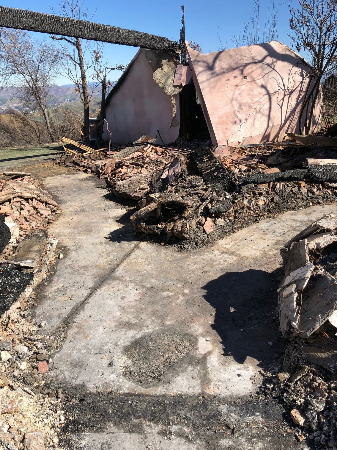 Charred remains of a building after a fire, with debris and a partially standing pink wall.