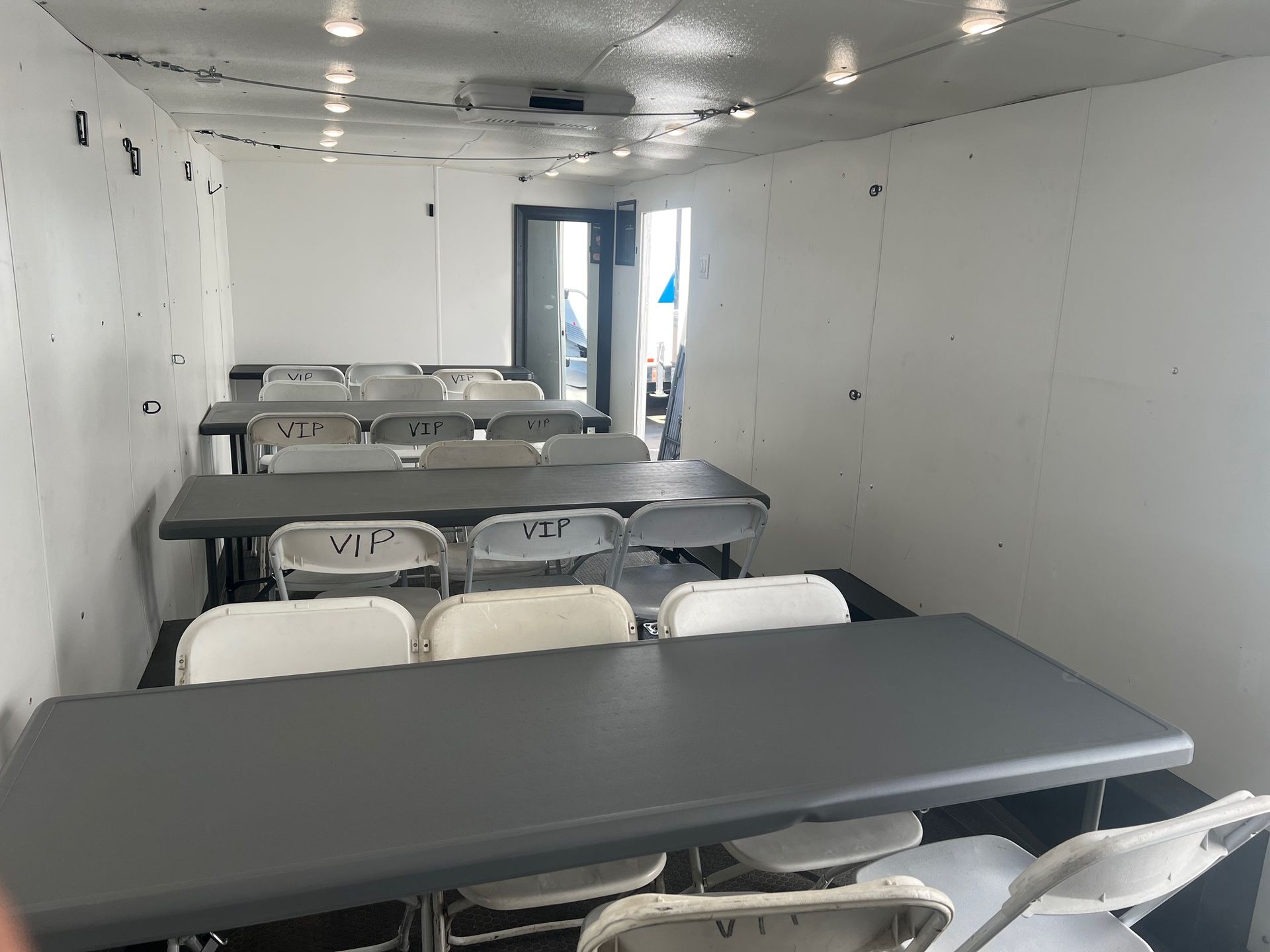 Classroom with tables and chairs, white walls, and a door to another room.
