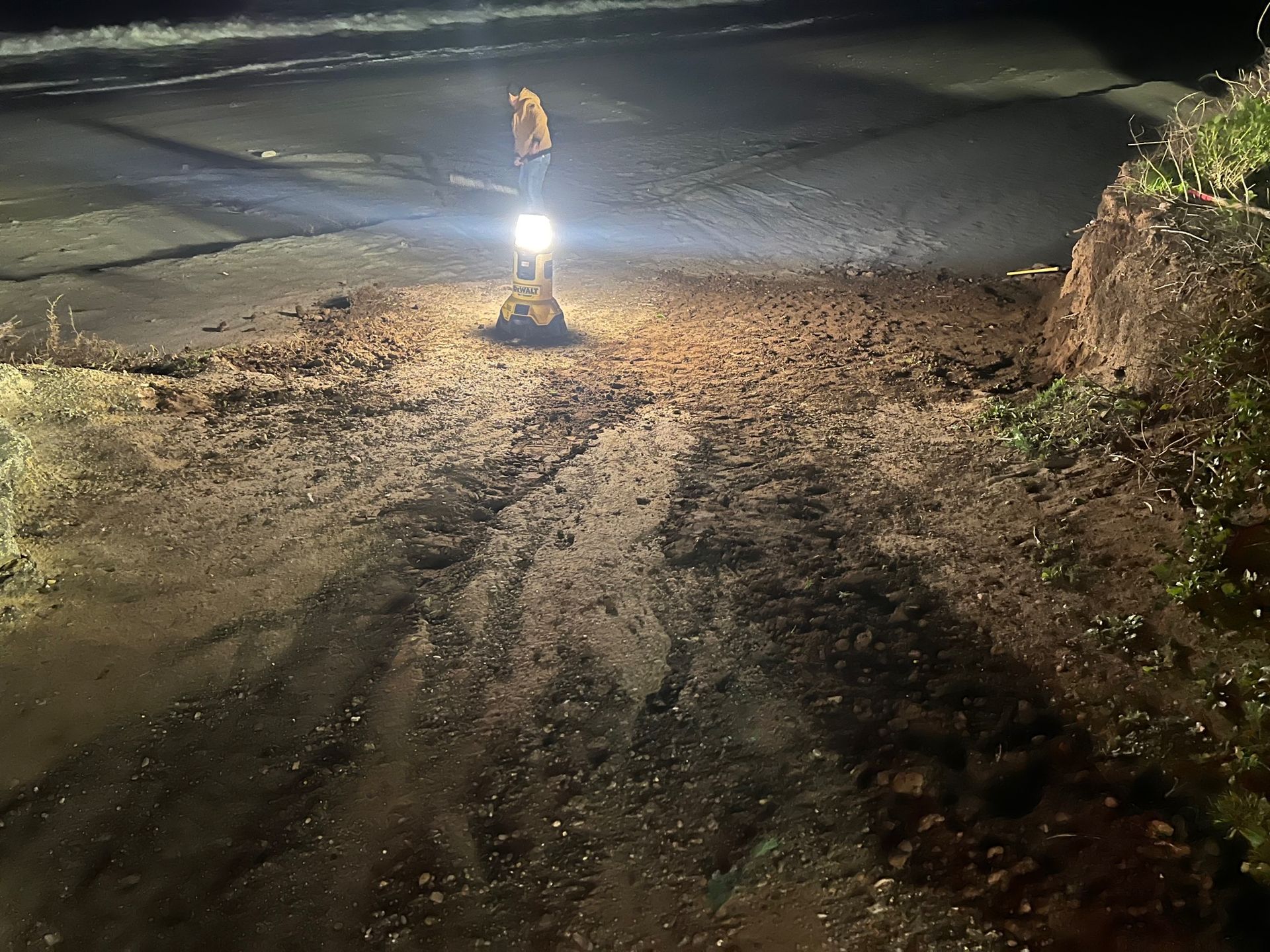 Excavator on a dark road, illuminated by its work lights, removing debris.