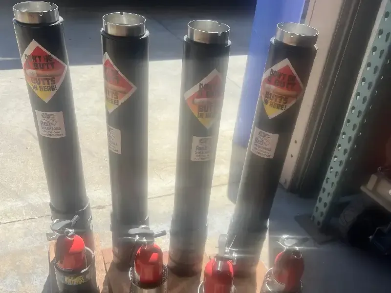 Four tall, black cylinders with red and white hazard labels and red nozzles, indoors.