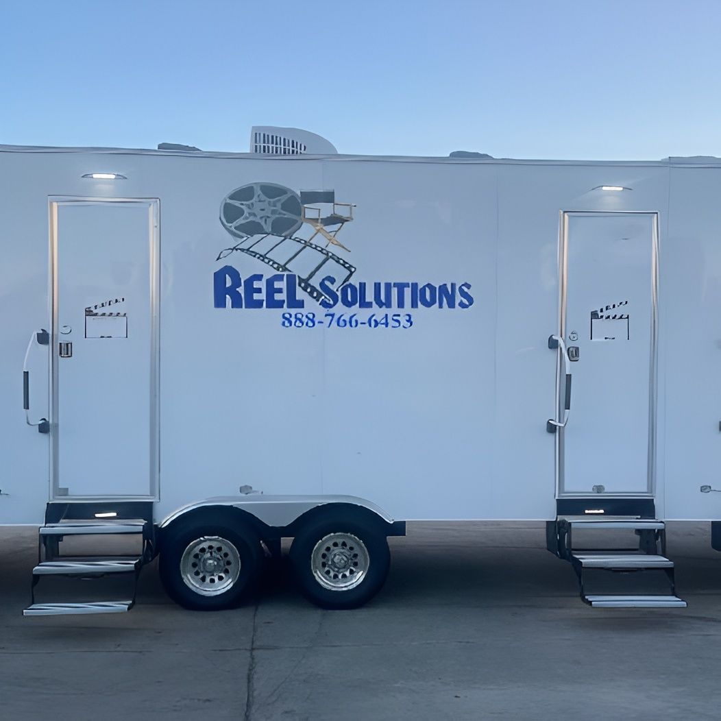 White trailer with two doors and Reel Solutions logo, parked outside.