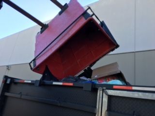 Red truck bed being unloaded, tilting up to dump contents.