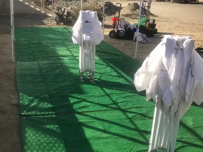 Green turf path with folded white canopy frames. Construction equipment visible in the background.