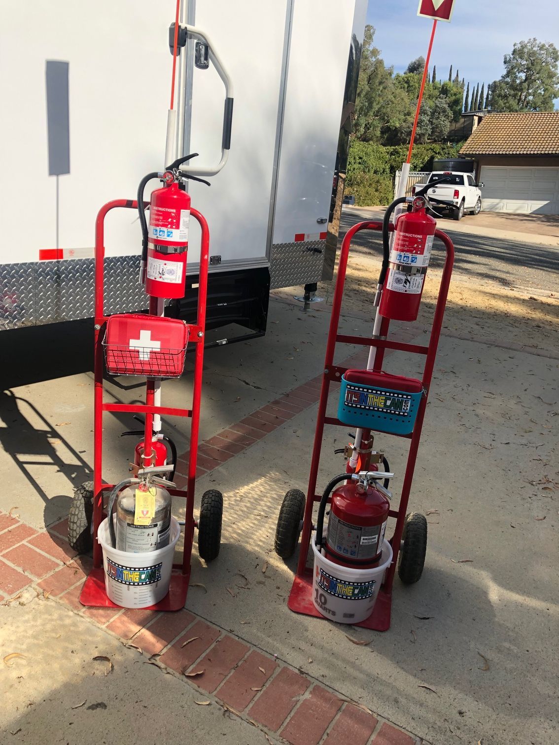 Two red carts with fire extinguishers and first aid kits outside, near a trailer.