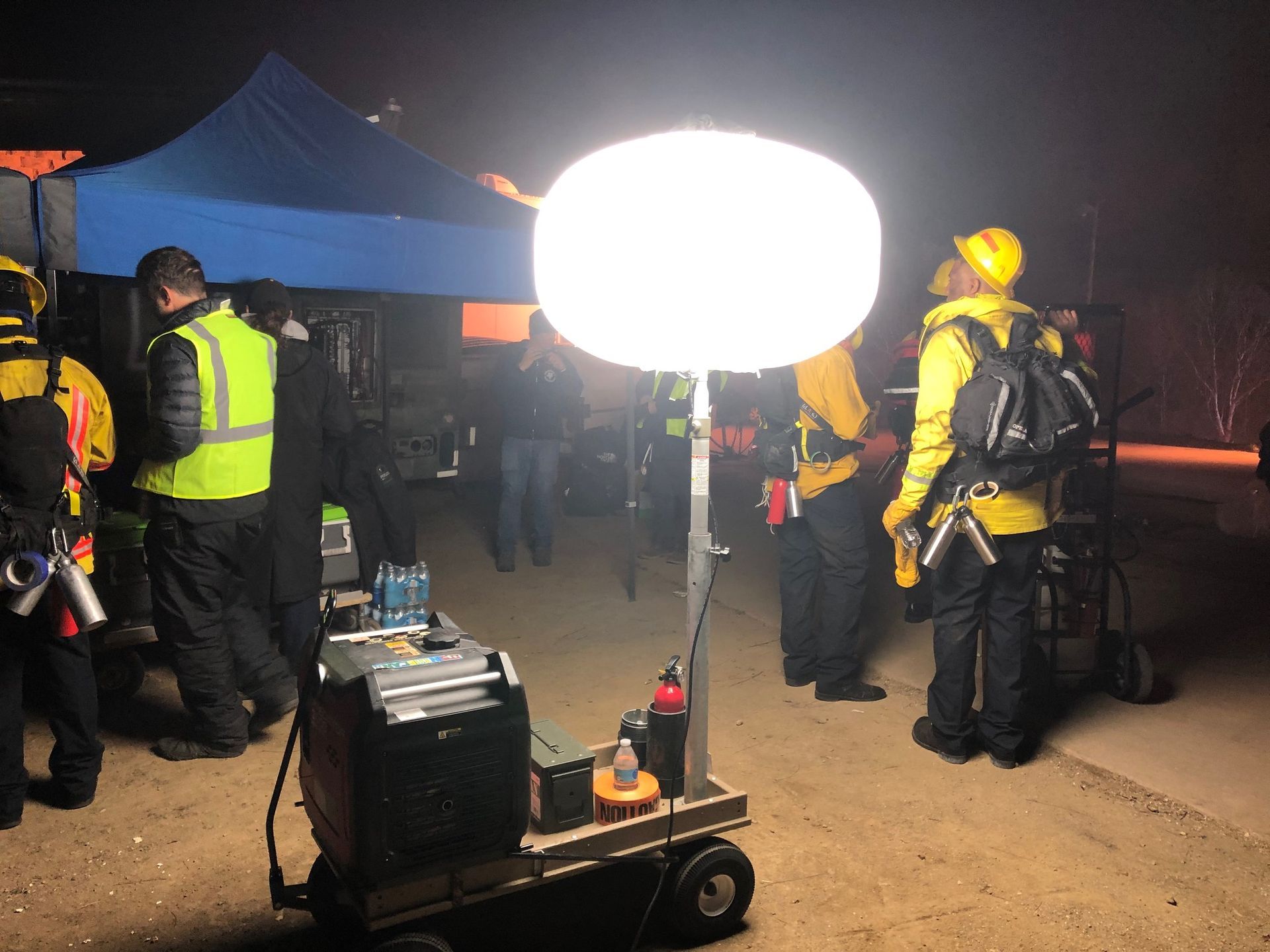 Emergency workers illuminated by a bright, portable light, outdoors at night.